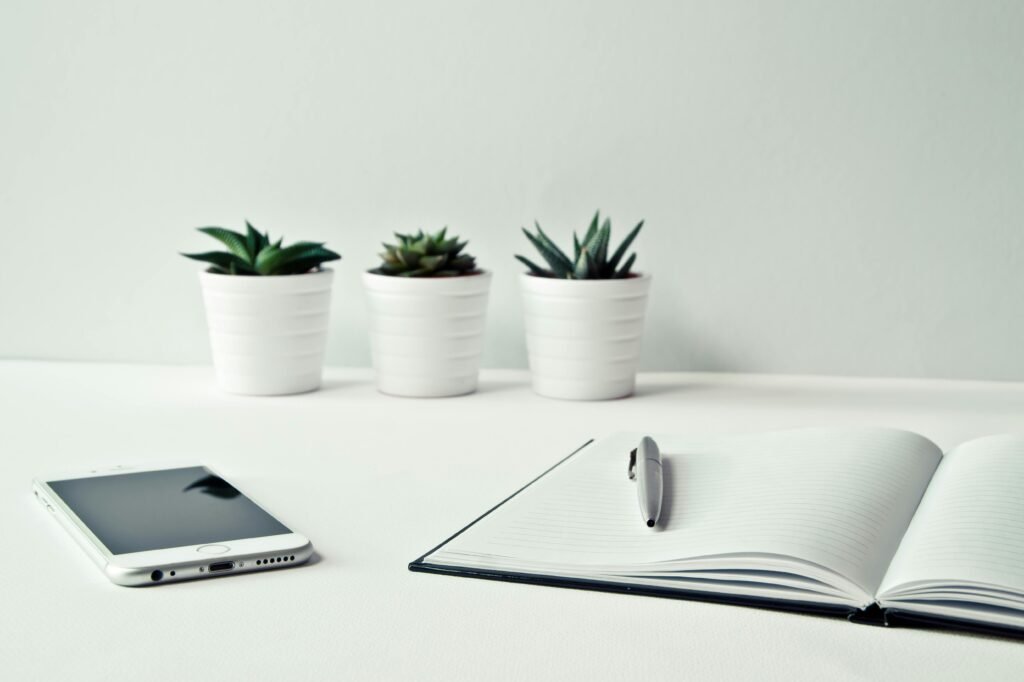 pexels-photo-796602-796602 A clean, minimalist workspace featuring a smartphone, open notepad, pen, and potted succulents.